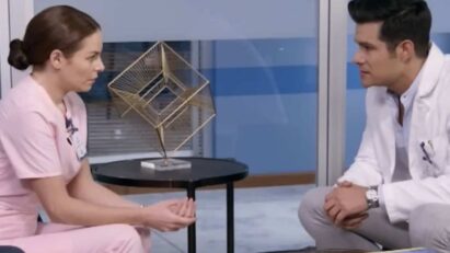 Ângela, com olhar sério e determinado, conversa com Leonardo em seu consultório. A expressão de Leonardo é de choque e incredulidade, enquanto a sombra de Mirtes paira sobre eles, simbolizando o mistério e a tensão que cercam a revelação.