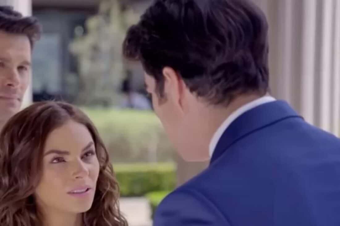 Ângela e Leonardo se olham com amor, enquanto Álvaro observa com amargura ao fundo.