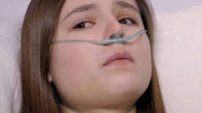 Clarinha deitada em uma cama de hospital, com os olhos abertos e um sorriso fraco no rosto. Álvaro, Dário e Flávia a observam com surpresa e emoção.