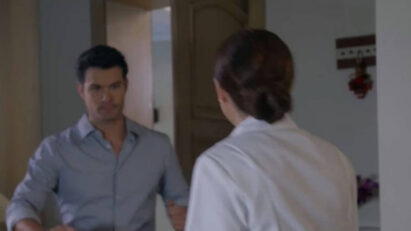 Ângela, com olhar triste e abatido, segura seus pertences enquanto sai da casa de Leonardo.