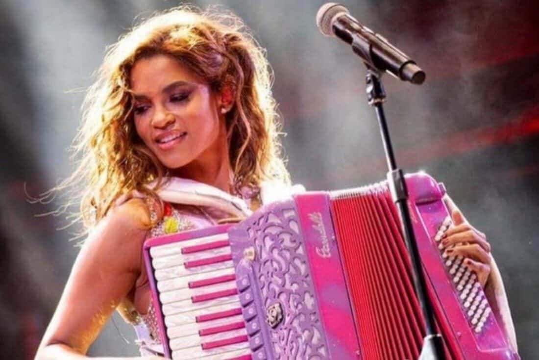 Lucy Alves como Lilith em Renascer, tocando sanfona com um sorriso no rosto e expressão apaixonada
