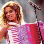Lucy Alves como Lilith em Renascer, tocando sanfona com um sorriso no rosto e expressão apaixonada