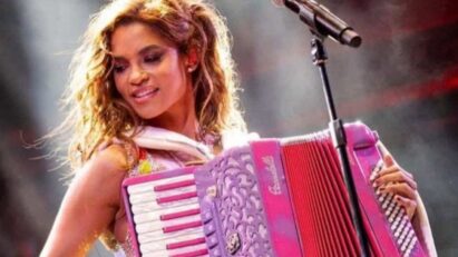 Lucy Alves como Lilith em Renascer, tocando sanfona com um sorriso no rosto e expressão apaixonada