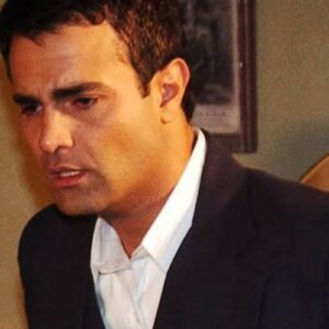 Cena de Alma Gêmea mostrando Roberval entregando uma caixa de presente para Dona Divina. Atrás deles, o clima é de festa de Natal, com decoração natalina.