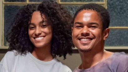 Cena de 'Renascer' mostrando Teca, uma mulher com um sorriso esperançoso, conversando com Pitoco, um homem olhando para ela com interesse.