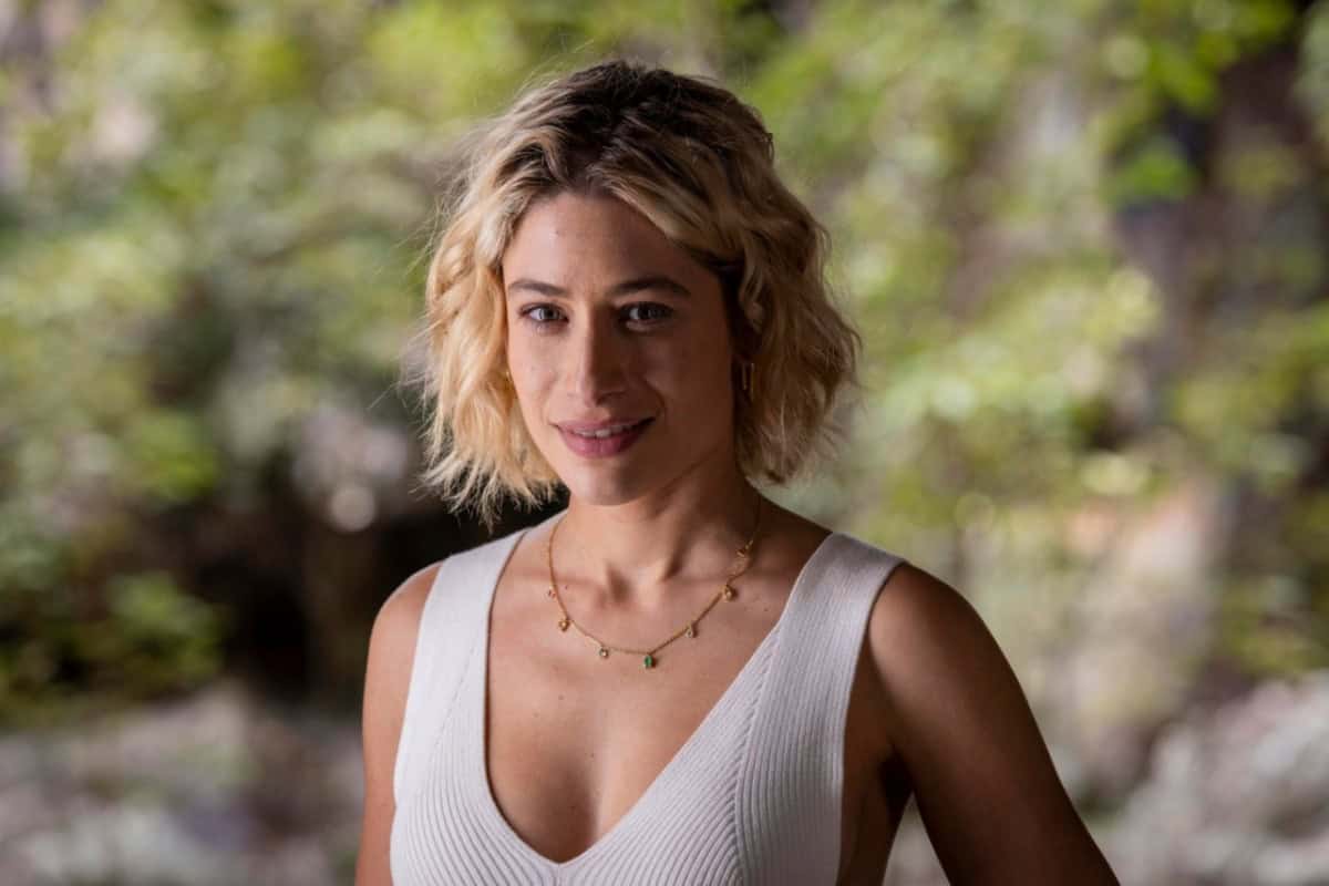 Blandina sorrindo de forma maliciosa, enquanto observa Quinota e Artur em uma situação tensa