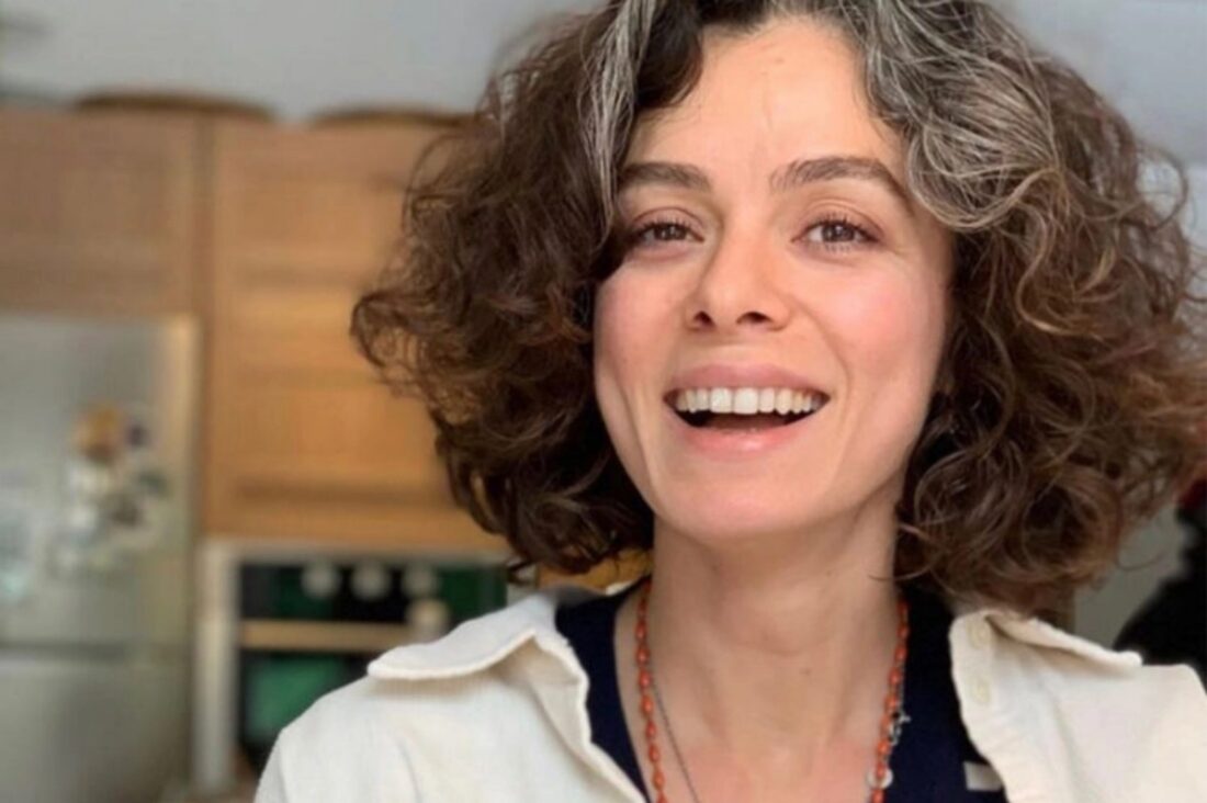 Imagem da atriz Özge Özpirinçci sorrindo, destacando seu amor pelos fãs brasileiros, com fundo de cena da novela Força de Mulher.