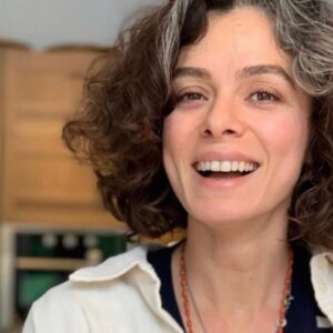 Imagem da atriz Özge Özpirinçci sorrindo, destacando seu amor pelos fãs brasileiros, com fundo de cena da novela Força de Mulher.