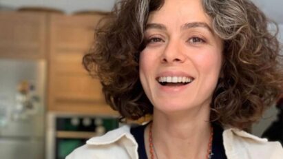 Imagem da atriz Özge Özpirinçci sorrindo, destacando seu amor pelos fãs brasileiros, com fundo de cena da novela Força de Mulher.