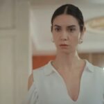 Cena da novela Força de Mulher, mostrando Piril pensativa, segurando o celular com a tela iluminada, demonstrando seu dilema.