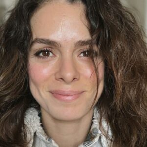 Foto de Özge Özpirinçci em um look preto, sorrindo e com um olhar expressivo.