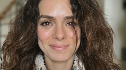 Foto de Özge Özpirinçci em um look preto, sorrindo e com um olhar expressivo.