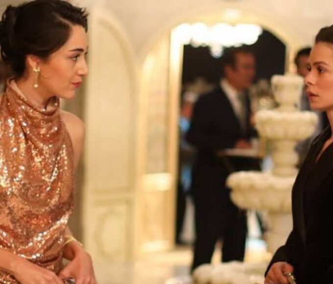 Bahar e Kismet trocando olhares tensos durante o evento em Força de Mulher, cena que revela conexão inesperada entre as personagens.