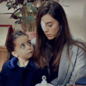 Zeynep com curativo no olho ao lado da menina Turna (Melek) e Gönul, na entrada da escola, em cena dramática da novela Mãe da Record.