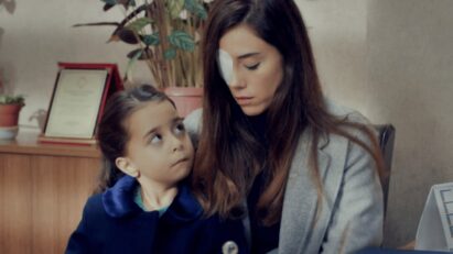 Zeynep com curativo no olho ao lado da menina Turna (Melek) e Gönul, na entrada da escola, em cena dramática da novela Mãe da Record.