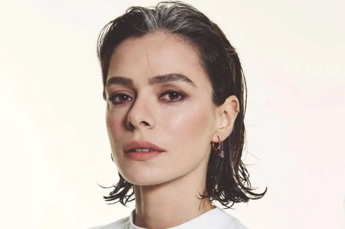 Özge Özpirinçci sorrindo em evento internacional com look natural.